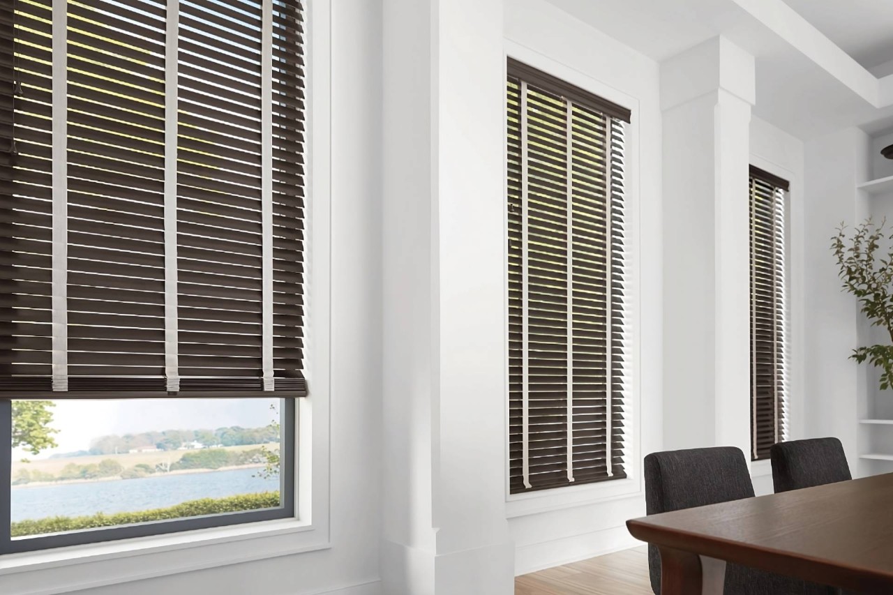 Hunter Douglas Parkland® Wood Blinds on tall dining room windows, overlooking a serene view at Eagle Harbor Window Coverings near Bainbridge Island, WA