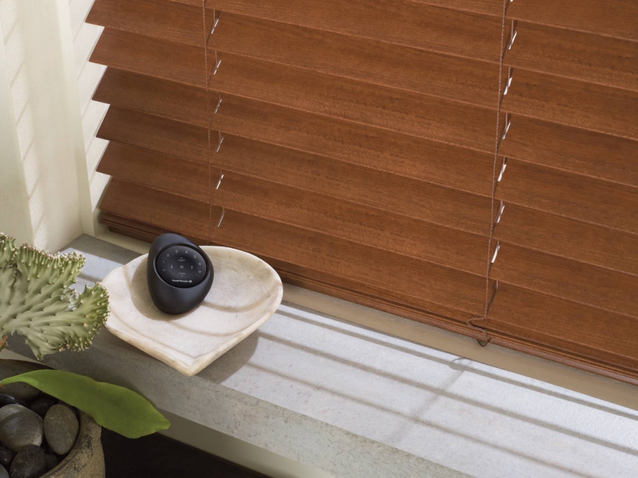 Hunter Douglas PowerView® Automation Pebble® Remote sitting on a windowsill by EverWood® Faux Wood Blinds at Eagle Harbor Window Coverings near Bainbridge Island, Washington (WA)